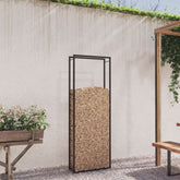 A tall, rectangular black steel firewood rack filled with logs sits on a gravel patio.